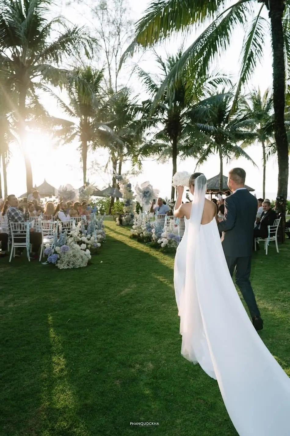 Bride and groom walking the aisle under palms as their guests look on