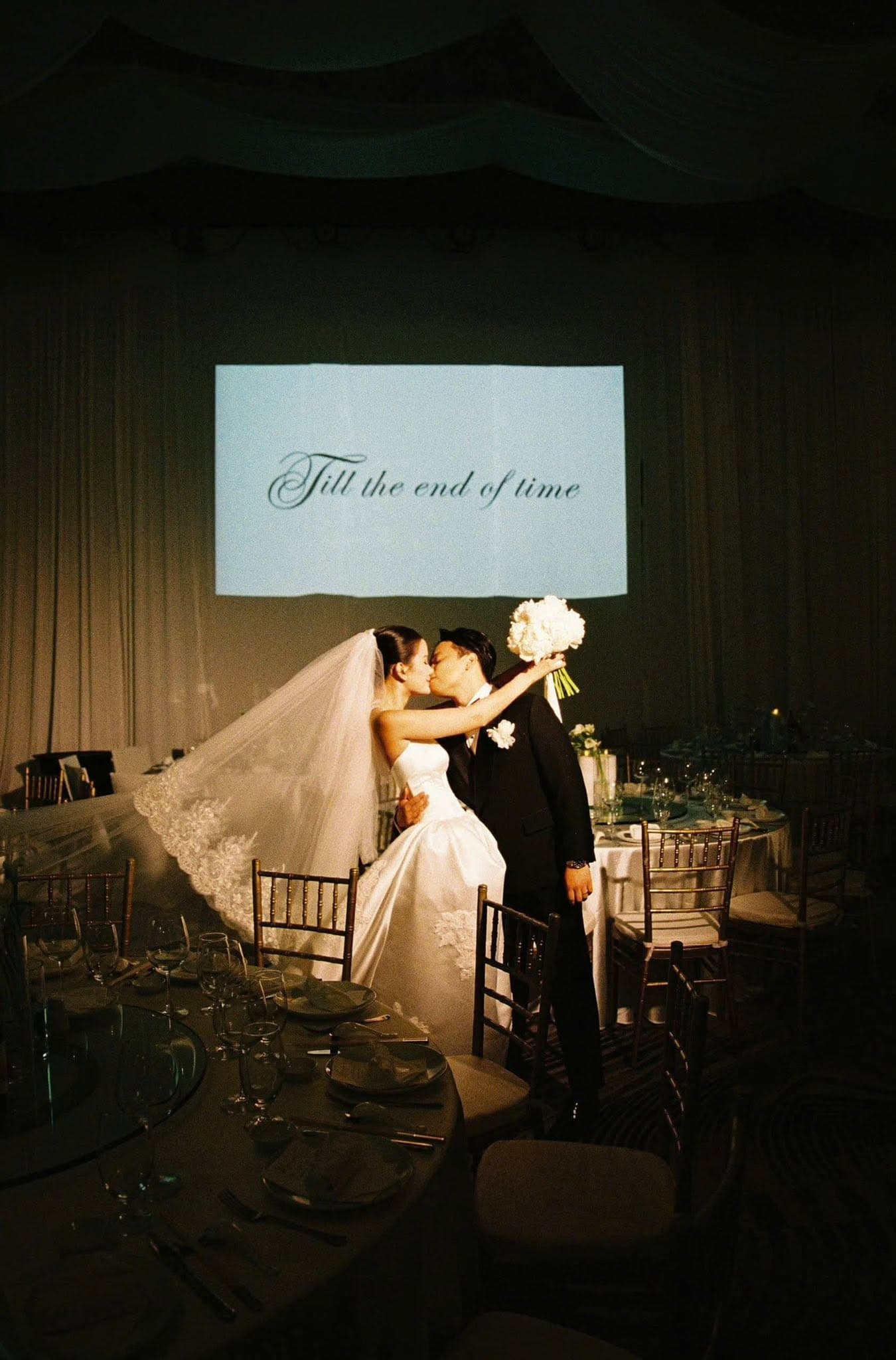 A couple kissing at their reception beneath a projected vow